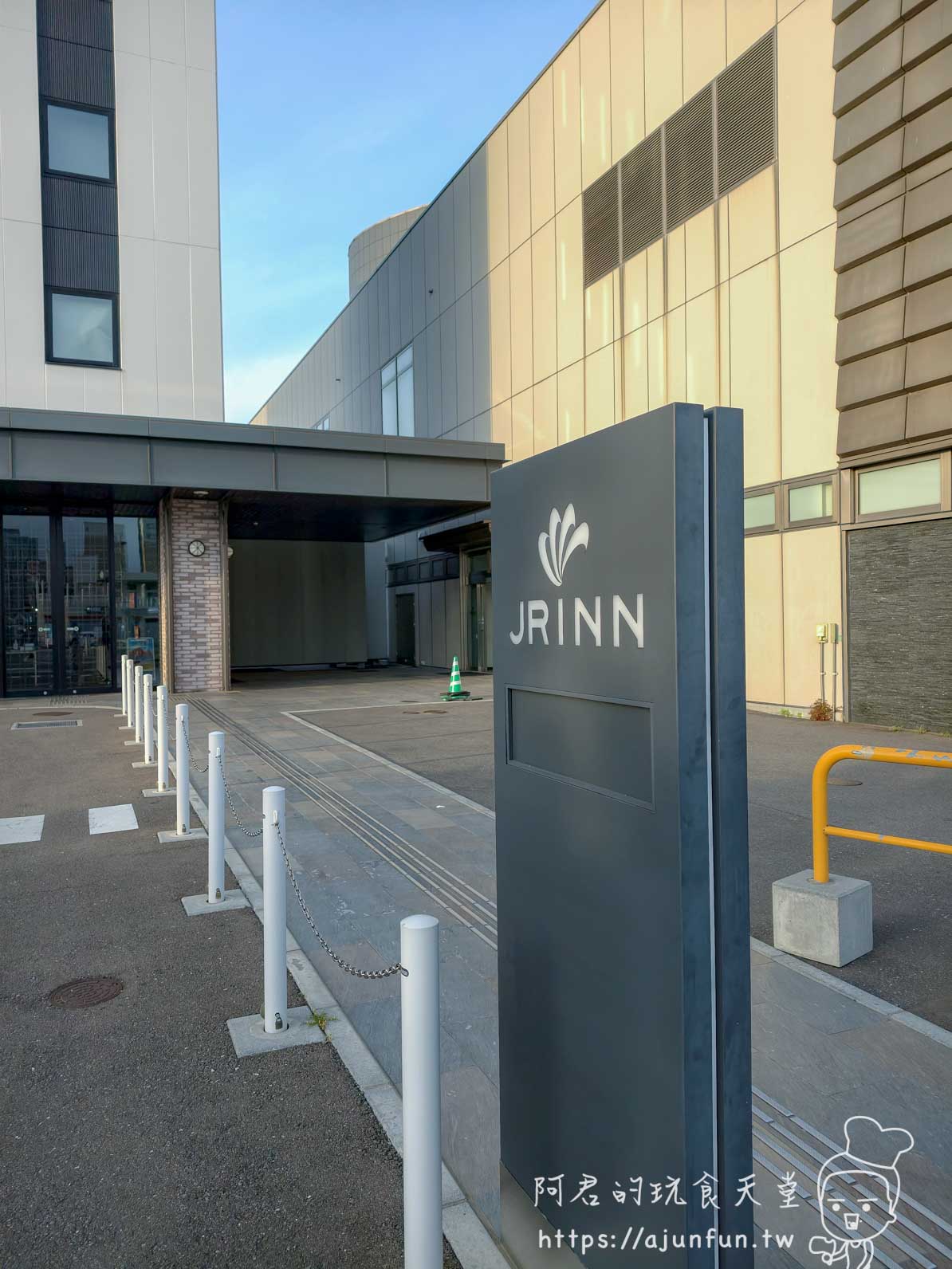JR INN 函館 戶外入口的深灰色 JR INN 花朵標誌立牌與多色外牆建築 - 阿君的玩食天堂