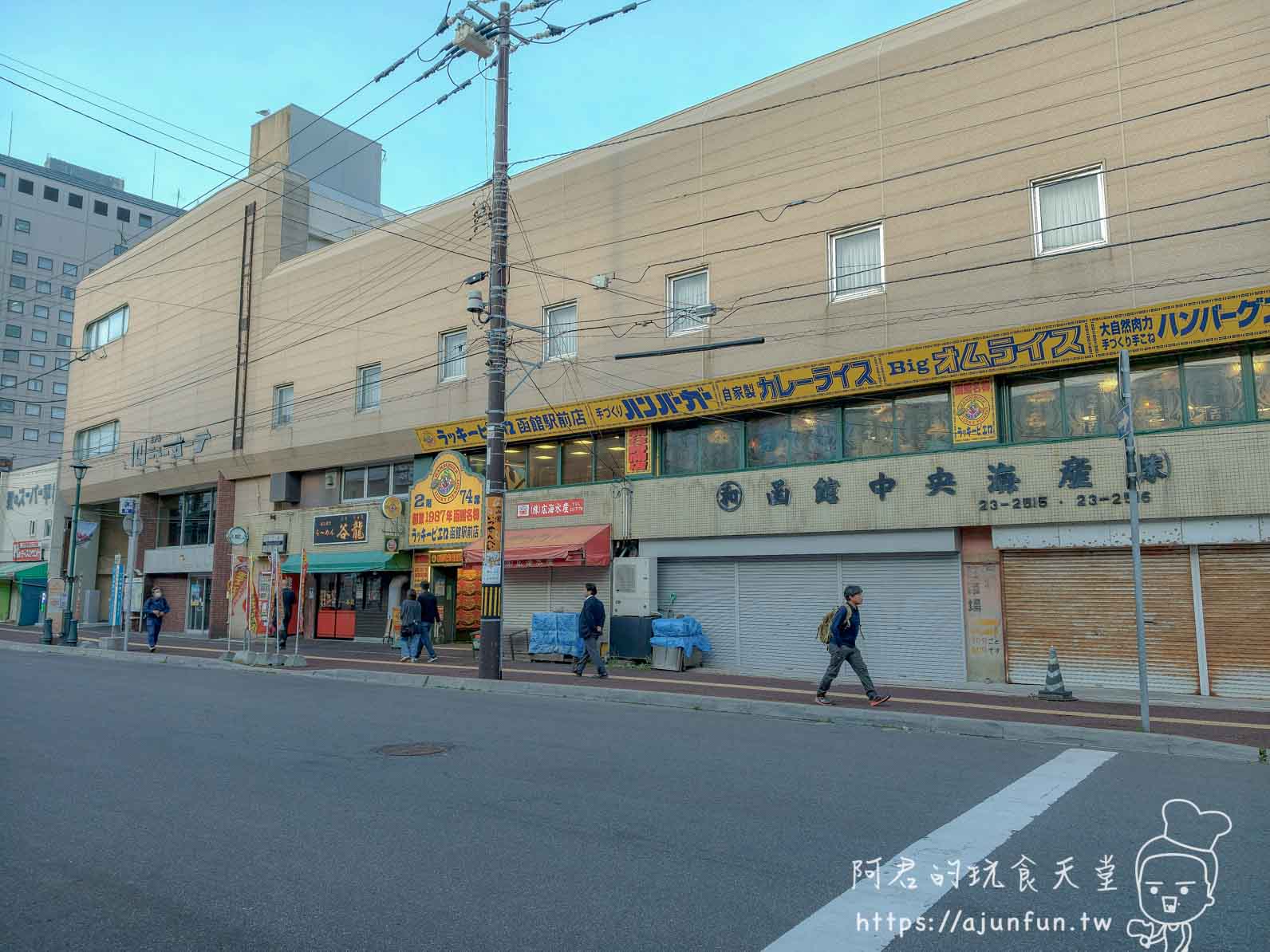【函館必吃】幸運小丑漢堡 函館駅前店|中華炸雞堡必點、價格菜單與排隊攻略2026 - 第1張圖 ラッキーピエロ 函館駅前店 外觀街景遠拍米色磁磚建物黃底招牌 - 阿君的玩食天堂